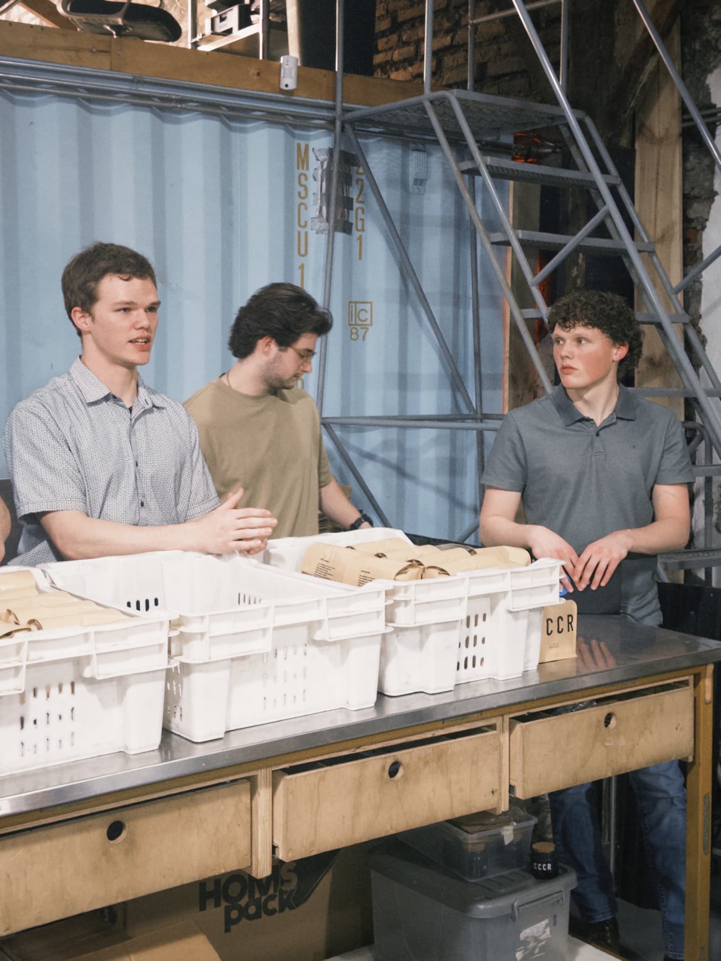 Three fellows working over coffee bags at a stainless steel table